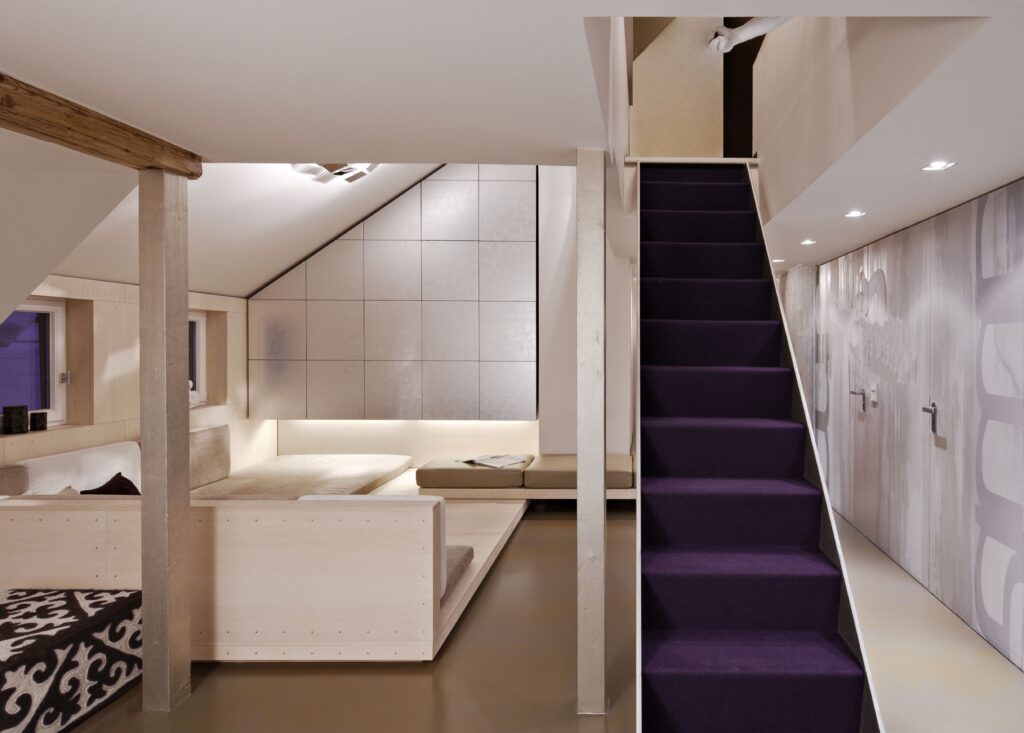 Finished basement renovation with built-in seating, concrete panel accent wall, purple carpet staircase and recessed lighting