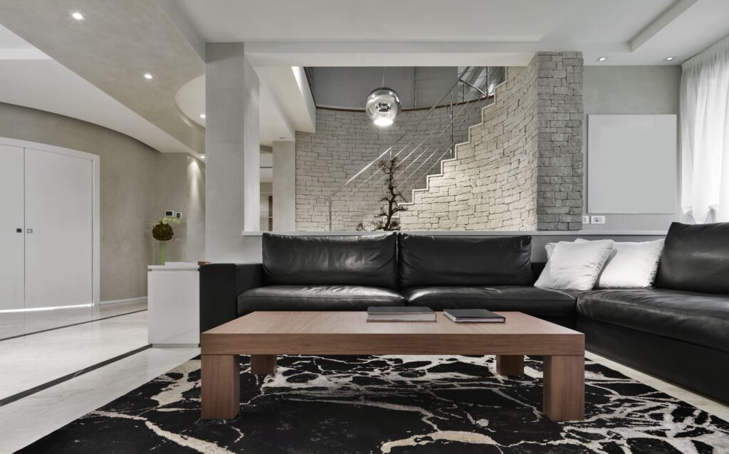 Modern finished basement with black leather sectional sofa, stone accent staircase wall and recessed ceiling lighting