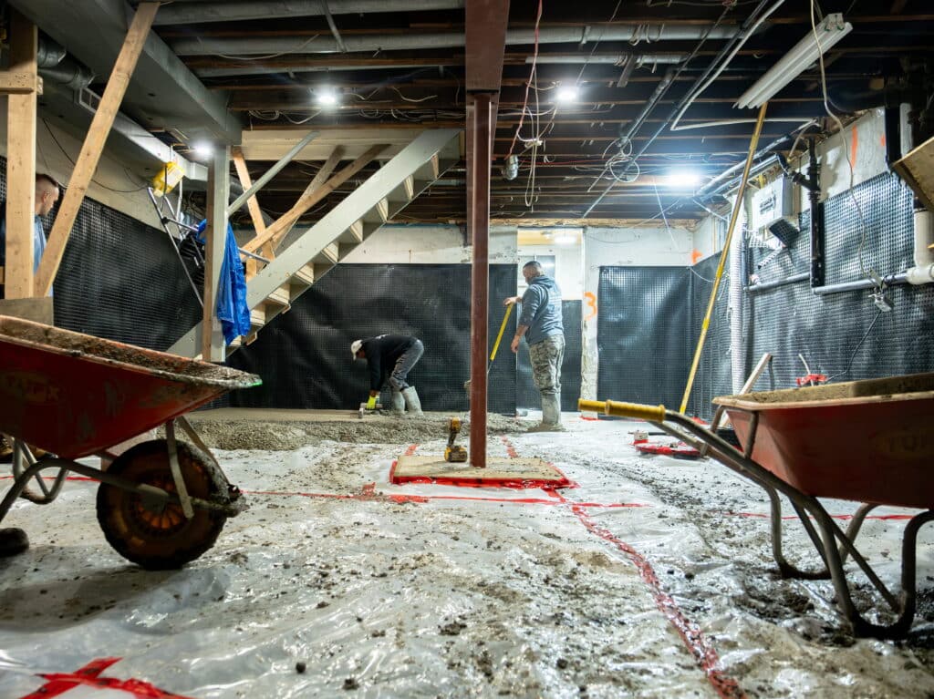 WillFix crew working on basement underpinning in Toronto — workers leveling concrete with wheelbarrows and waterproofing membrane visible on walls