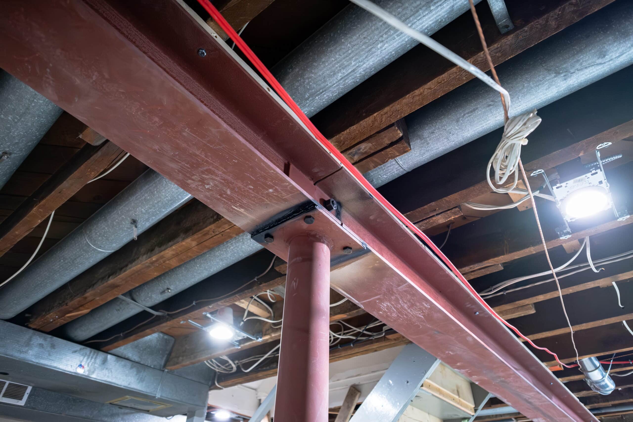 basement-underpinning-toronto-structural-construction-willfix Steel I-beam supported by lally column in basement ceiling after load-bearing wall removal during structural construction