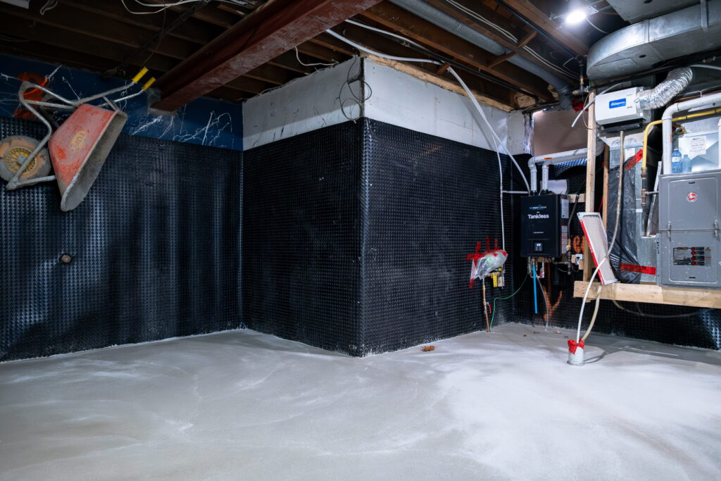 Basement interior with dimple mat waterproofing membrane on corner walls, new concrete floor and tankless water heater