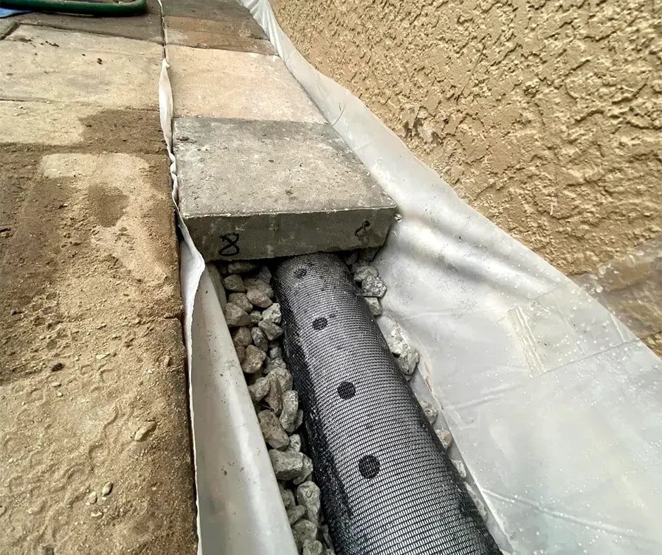 French drain installation with perforated pipe, gravel bed and geotextile fabric liner along exterior house foundation